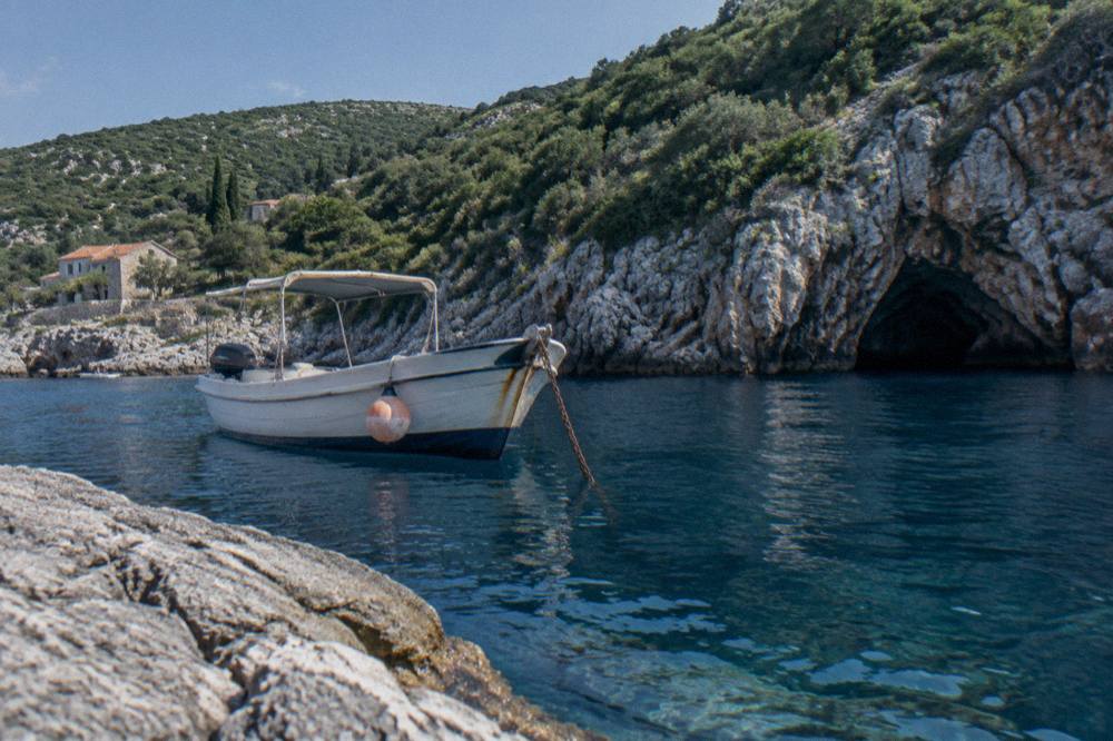 A small boat anchored near steep green cliffs above deep blue water in the Bay of Kotor