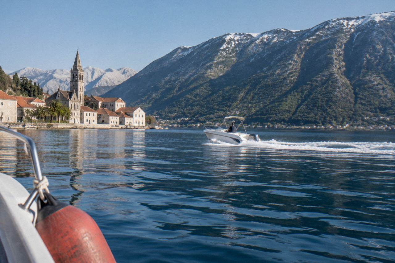 A speedboat crossing calm blue water in the Bay of Kotor with green mountains behind