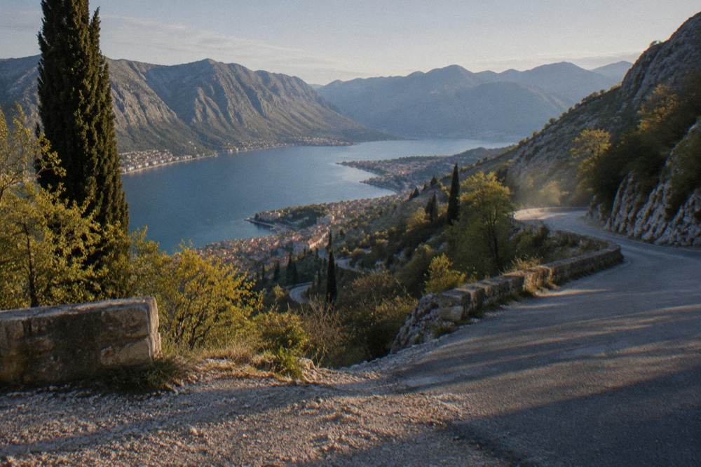 Winding two-lane road curving along a forested mountainside above blue sea