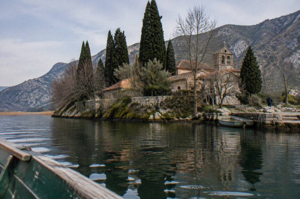 Small stone monastery building on a wooded islet in Lake Skadar seen from the water