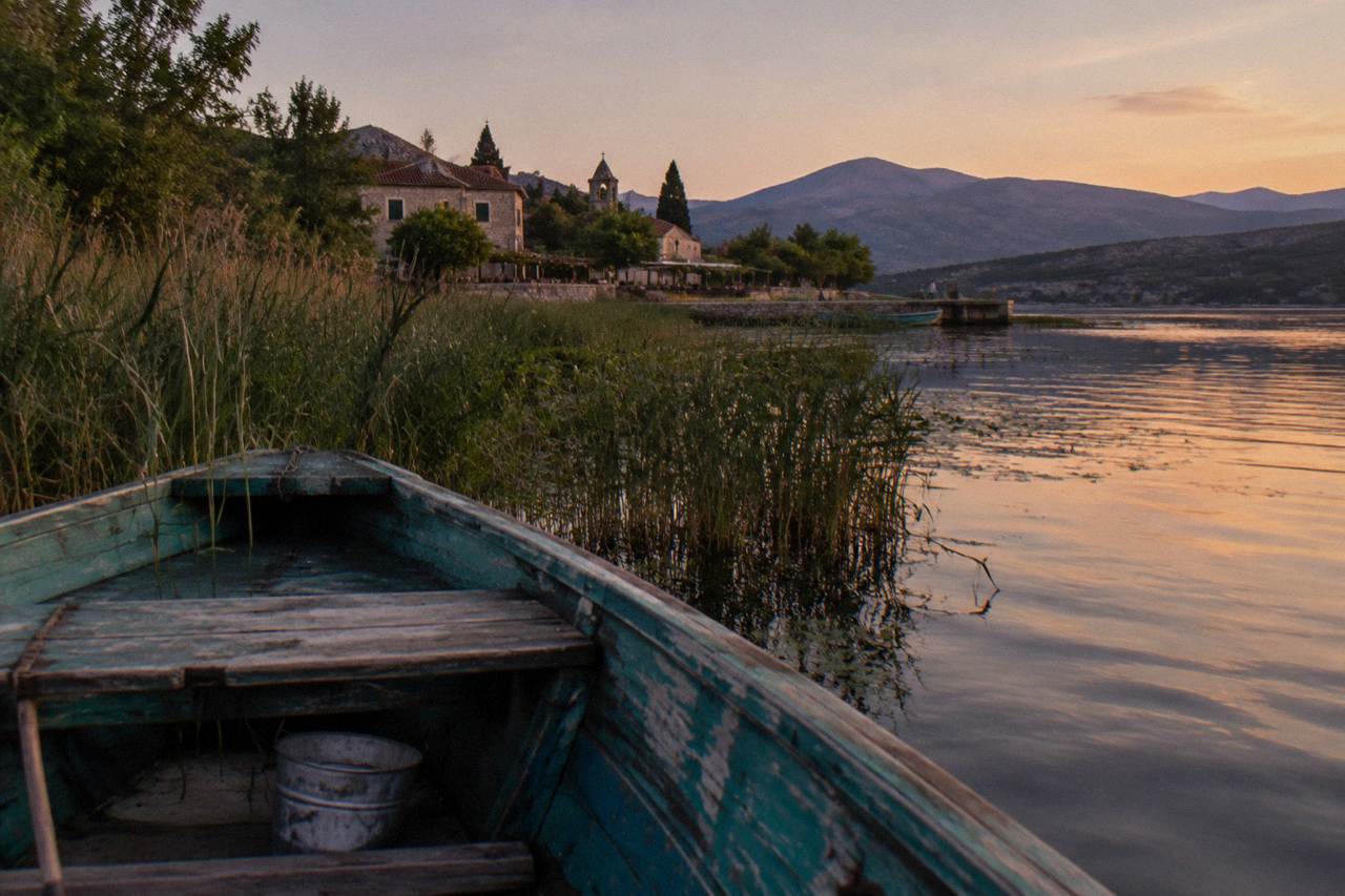 Wooden boat moored on calm Lake Skadar water near reed beds and low hills