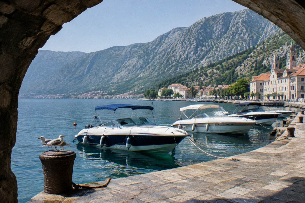 Speedboats moored on the water beside the walled old town of Kotor under a clear sky