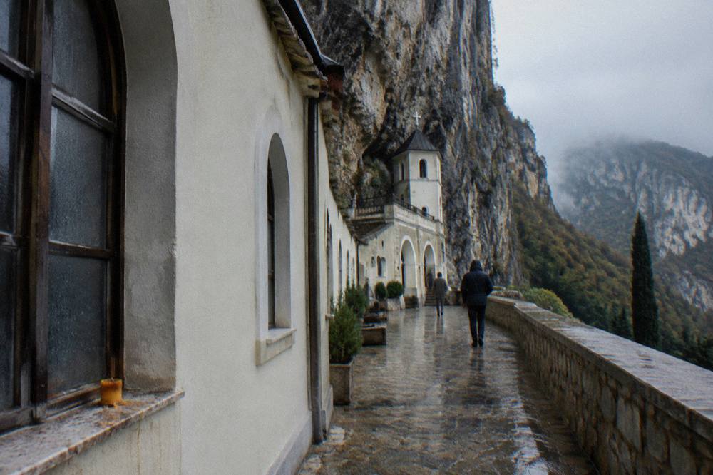 Pale monastery walls and arched windows set directly into a vertical grey cliff