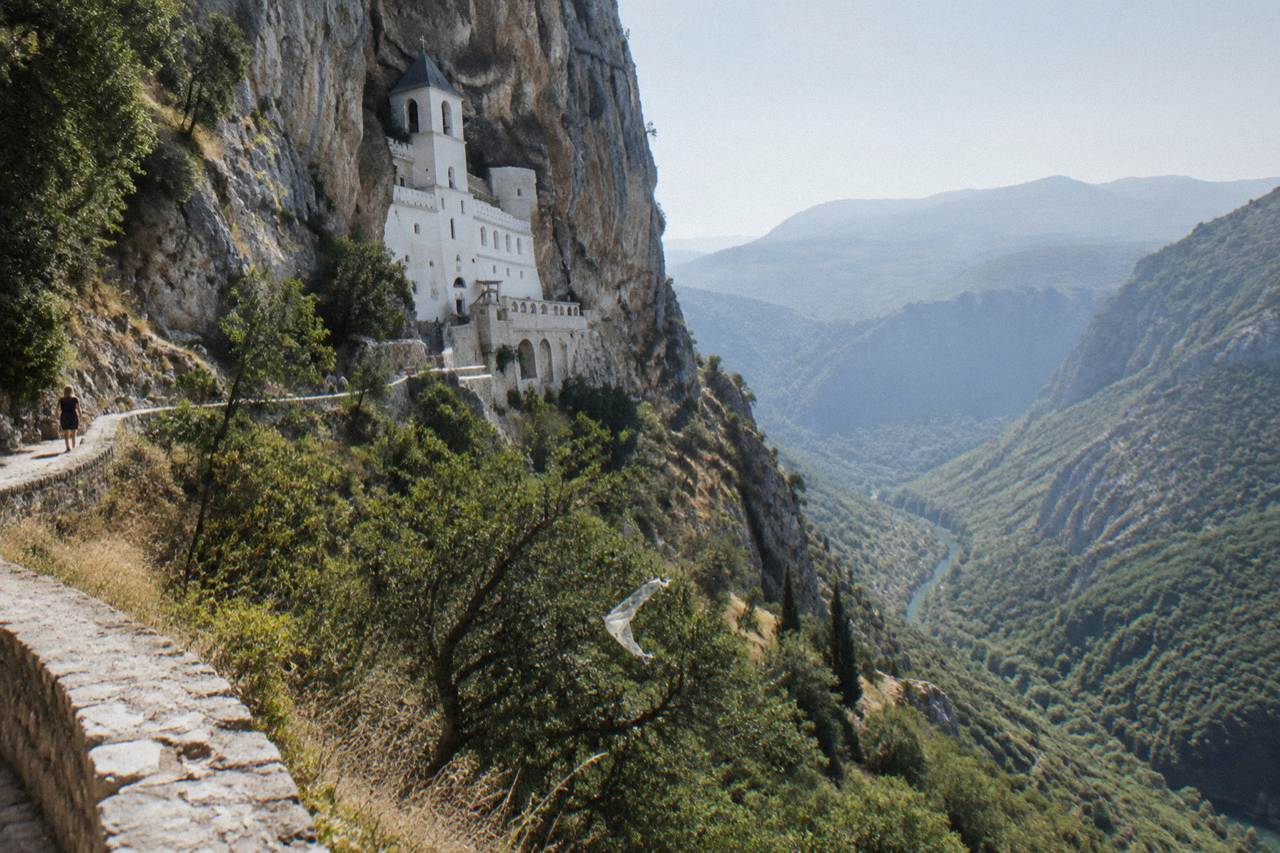 White monastery buildings built into a sheer cliff face above a green valley