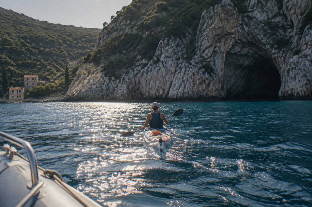 A single kayak paddling across open blue sea toward rocky cliffs in afternoon light