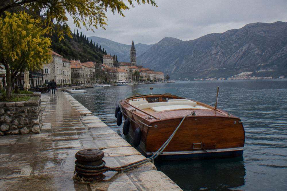 A wooden speedboat moored beside a stone quay with hills rising behind a bay