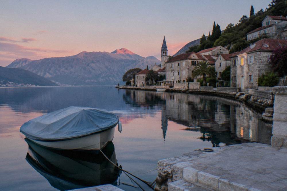 Calm bay water at dawn with mountains reflected and a speedboat moored at a dock