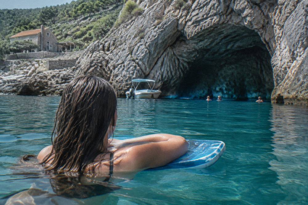 A swimmer holding a foam kickboard in turquoise water beside a rocky coastline