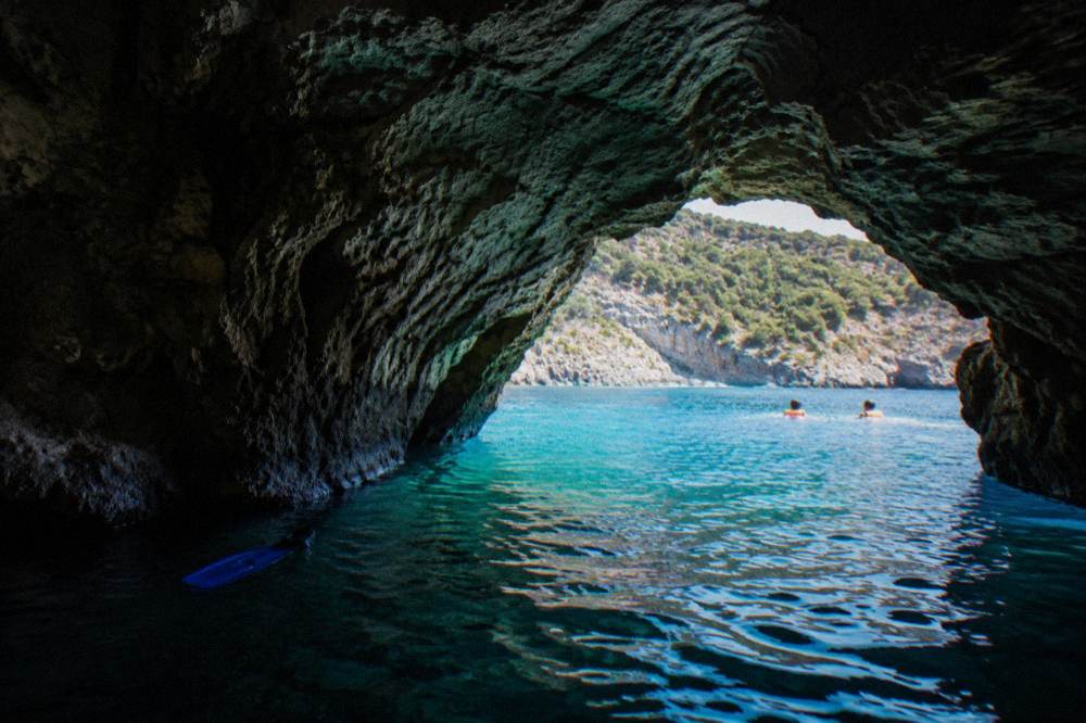 Turquoise water glowing inside a sea cave with swimmers floating near the entrance