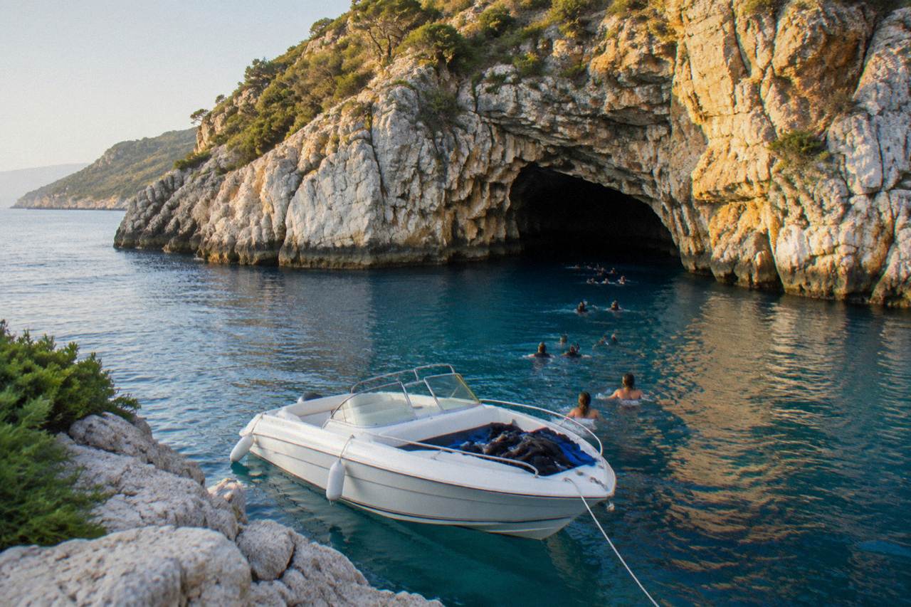 Speedboat anchored outside a glowing blue sea cave on the Lustica peninsula coastline