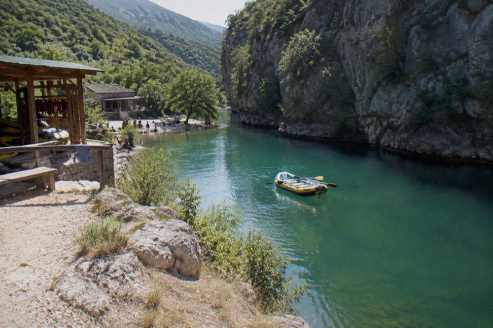 Empty raft floating on calm green river water beside a steep canyon wall