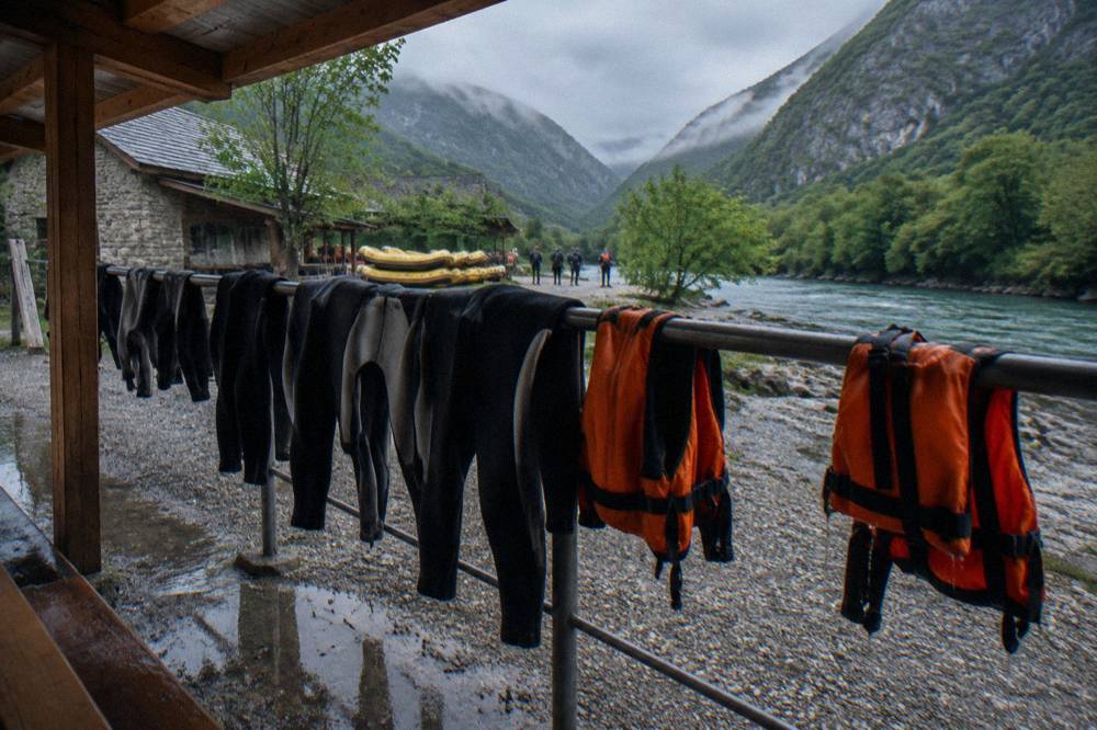 Neoprene wetsuits and life jackets drying on a railing beside a river camp