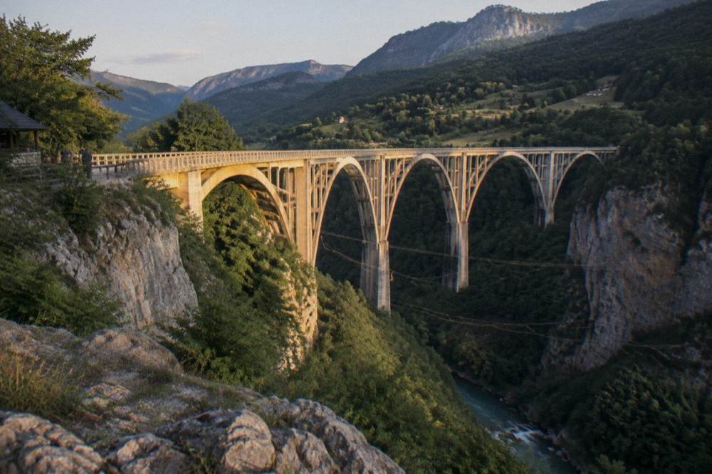 Arch concrete bridge spanning a deep forested river canyon under a clear sky