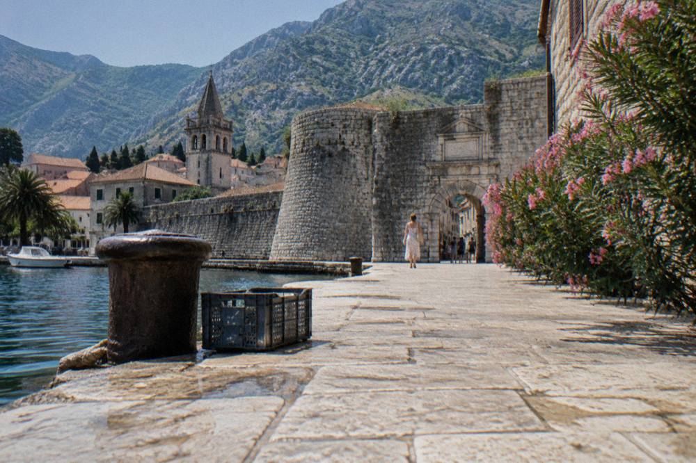 Flat stone waterfront promenade in Kotor leading toward the medieval Sea Gate and town walls
