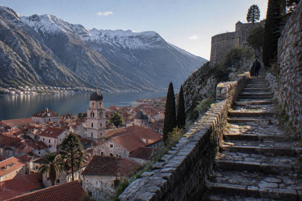 Stone stairway climbing the fortified walls of Kotor above red rooftops toward the hilltop fortress