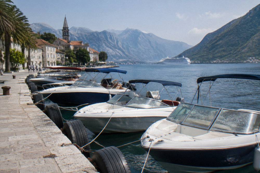 Speedboats moored on Kotor waterfront with cruise ship anchored in the bay behind