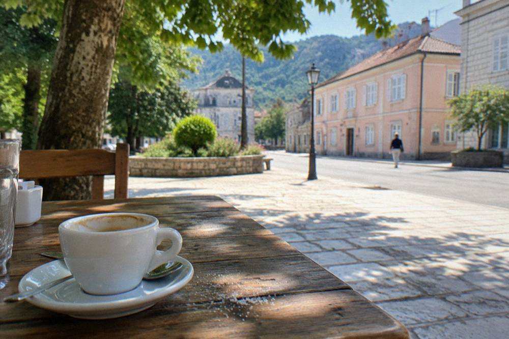 A wooden table with a printed menu and a coffee cup beside a sunny street in an old town