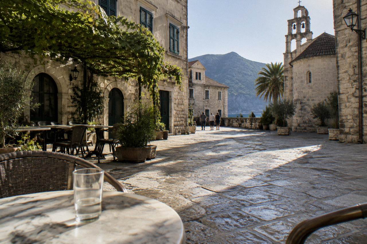 A stone paved square in a Montenegrin coastal old town with café tables and shuttered buildings