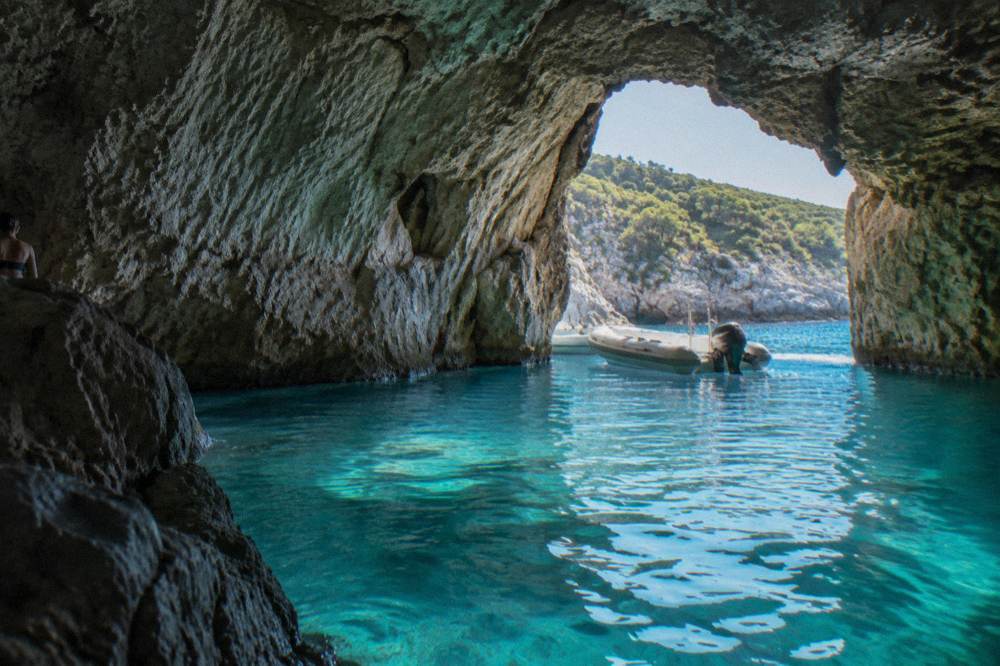 Turquoise water glowing inside a wide sea cave with a small boat waiting outside