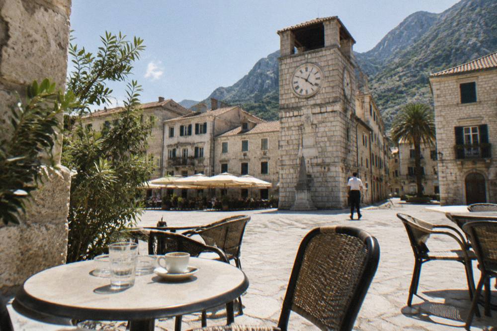 Sunny square in Kotor Old Town with cafe tables and old clock tower