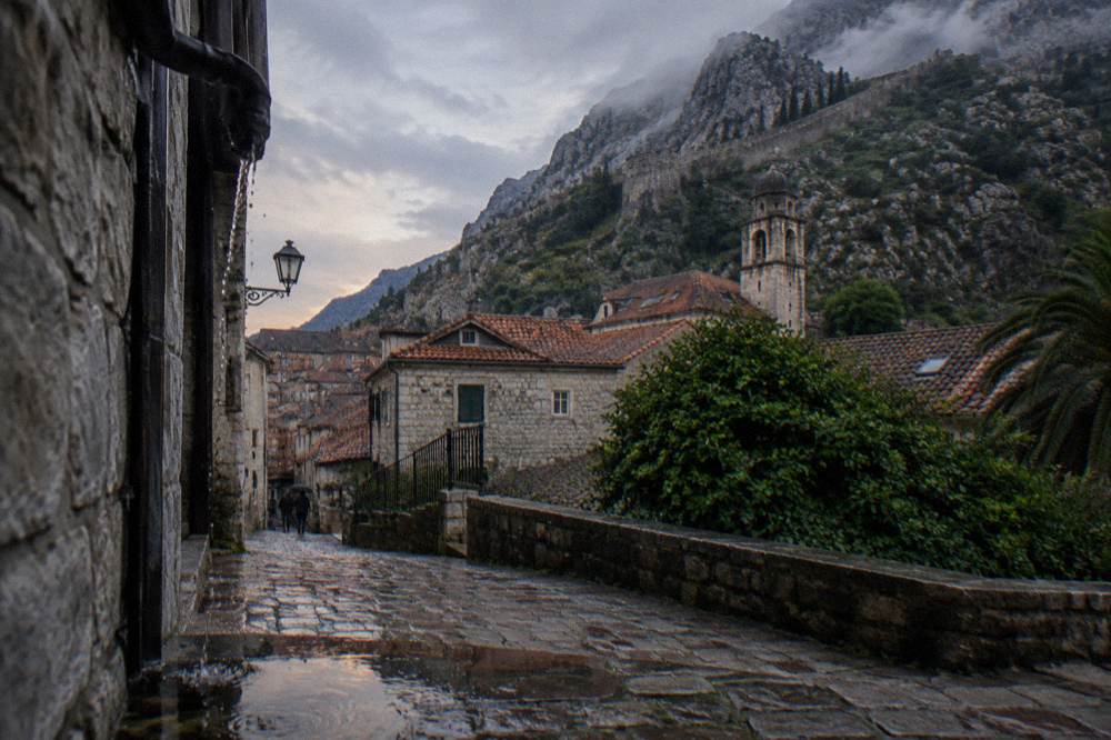 Ancient city wall rising above red rooftops of Kotor Old Town toward the hillside