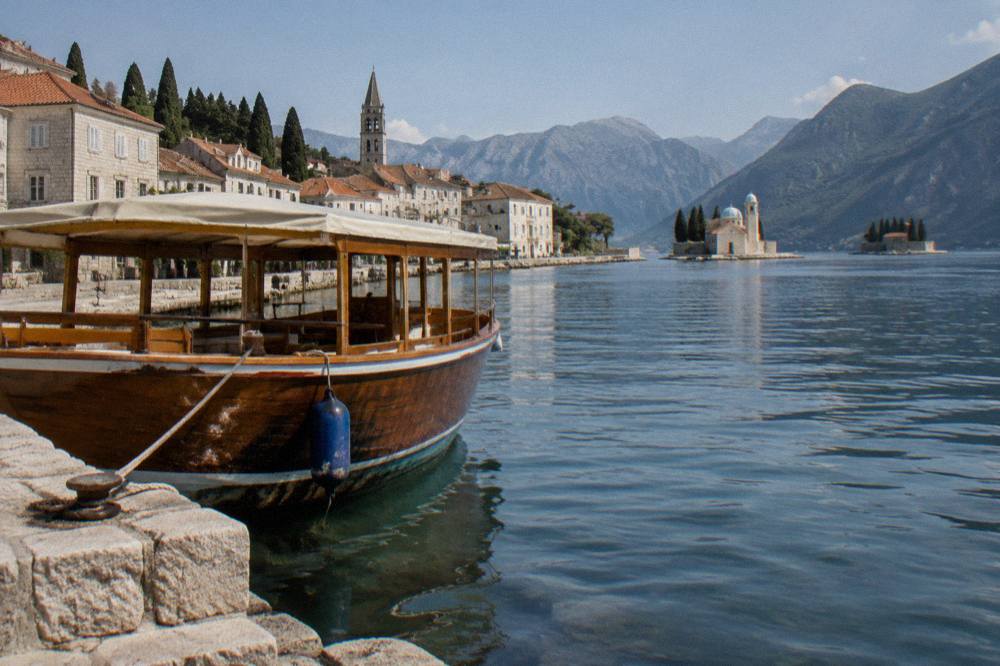 A wooden sightseeing boat moored beside the stone waterfront of Perast with island churches in the distance