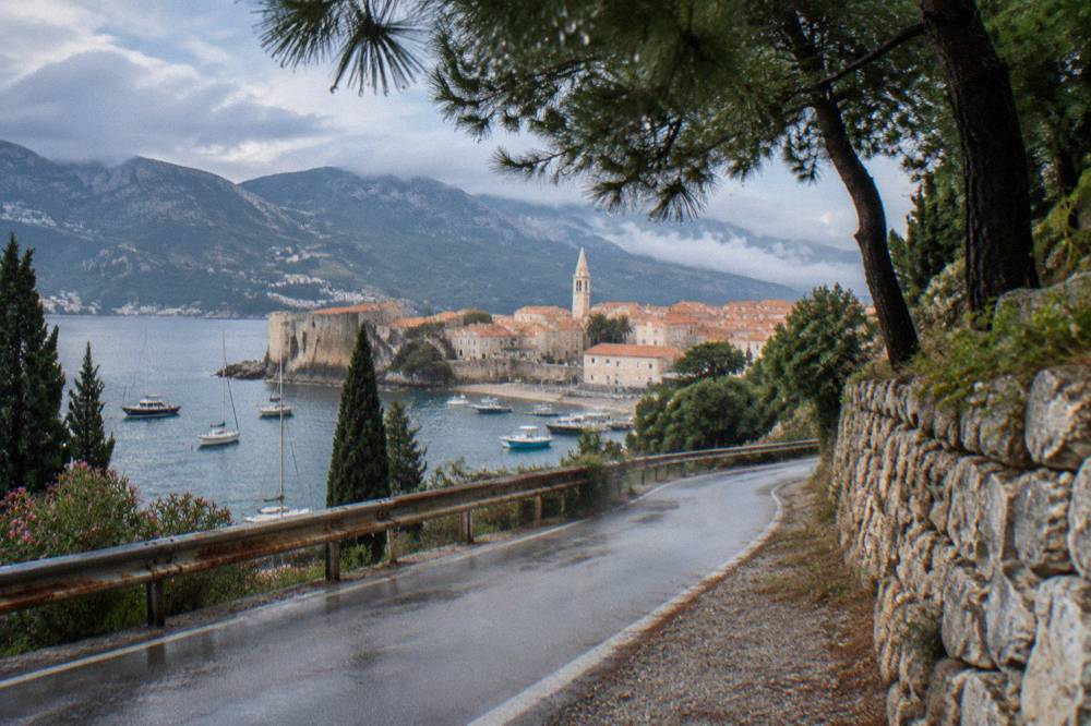 A coastal road curving along a hillside above boats anchored in a blue Adriatic cove
