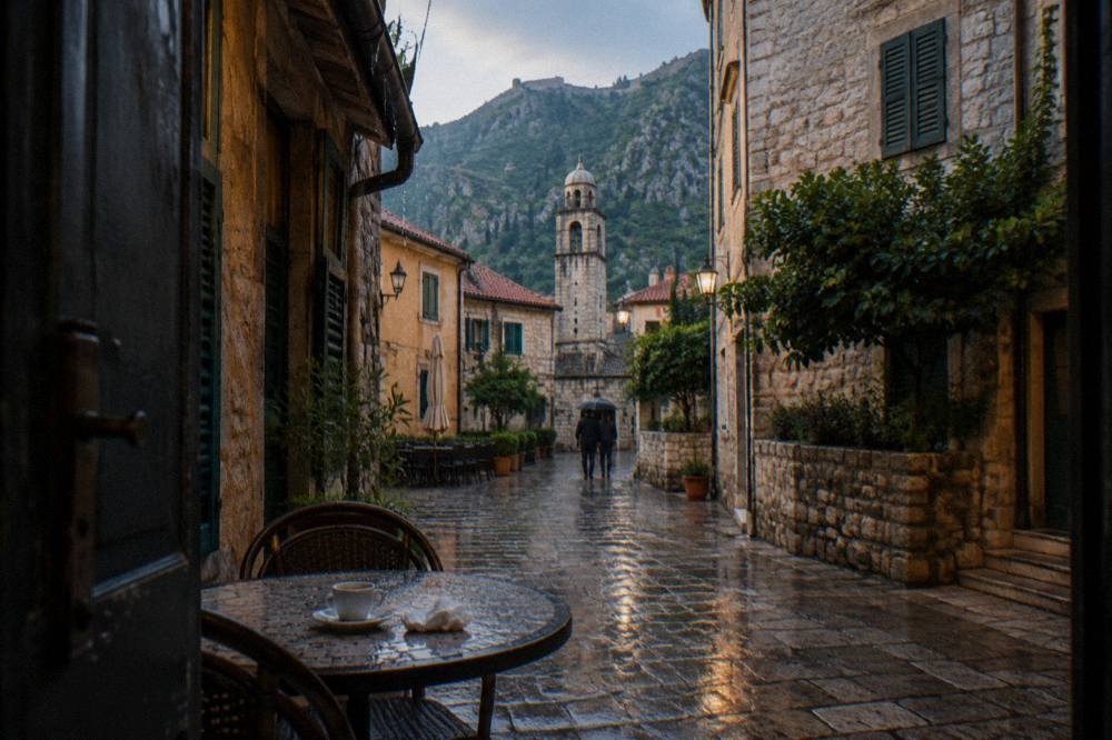 Narrow stone street inside a medieval walled town with shuttered houses and a café table