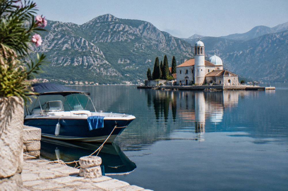 Blue speedboat anchored near a stone island church in a calm bay