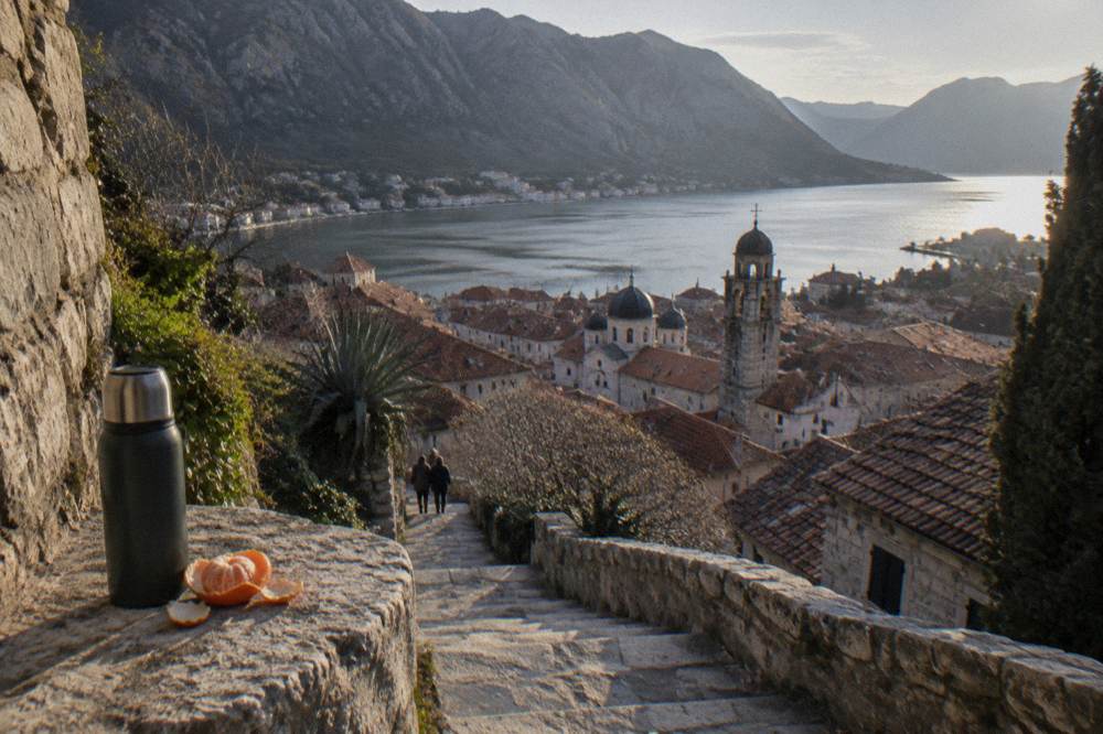 Walled town rooftops seen from a high stone fortress path above the bay