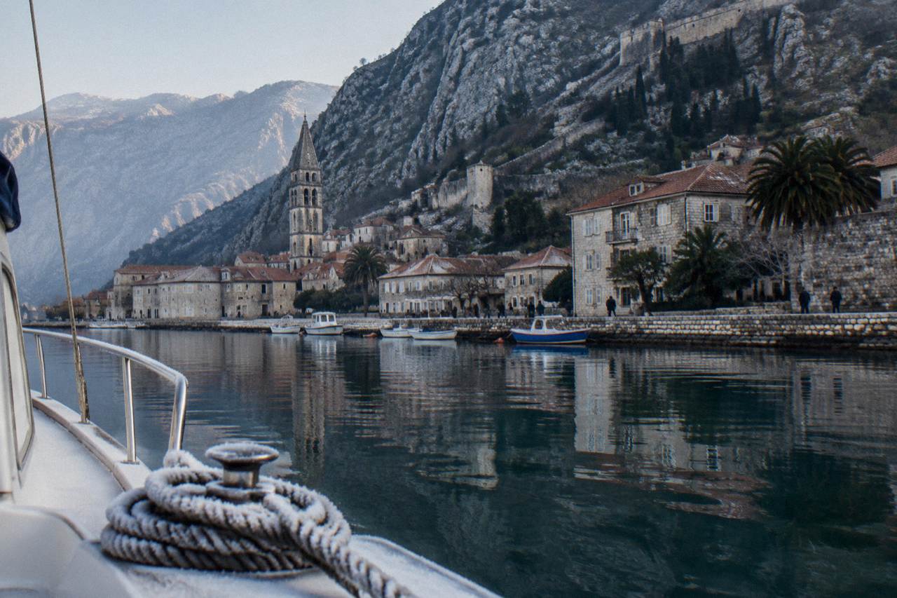 Stone ramparts of a walled Adriatic town rising above a fjord-like bay with moored boats