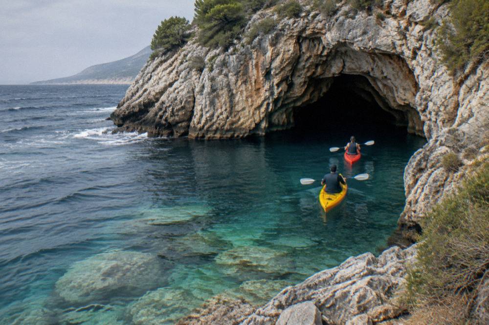 Sea kayaks paddling along a rocky coastline toward a cave opening in clear blue water