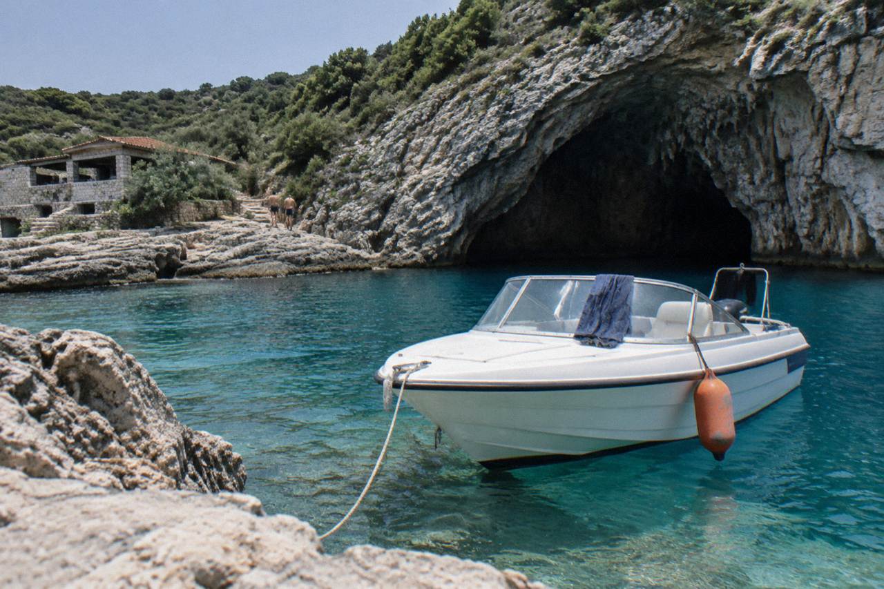A speedboat anchored on turquoise water near a seaside cave entrance on the Lustica peninsula coastline