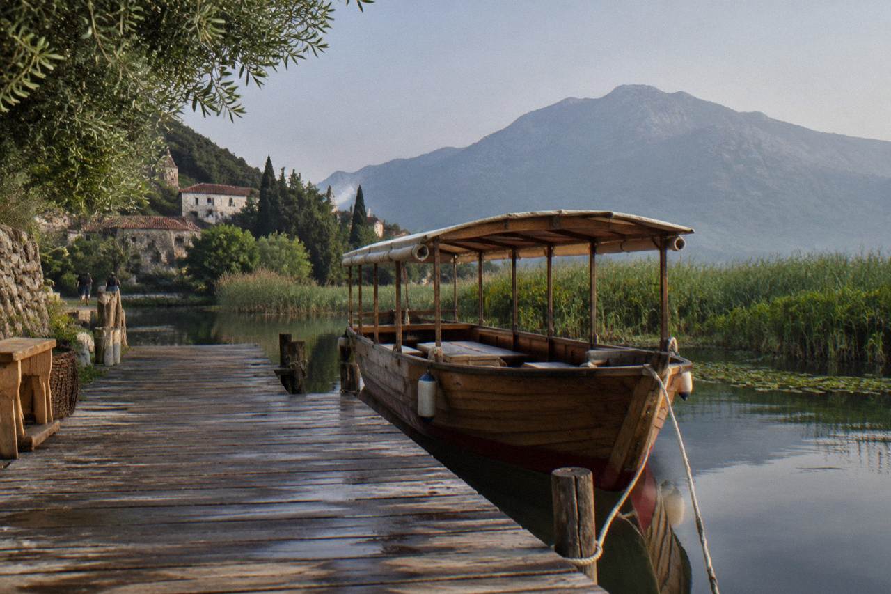 Wooden boat moored at a small jetty on a wide lake with reed beds and distant mountains