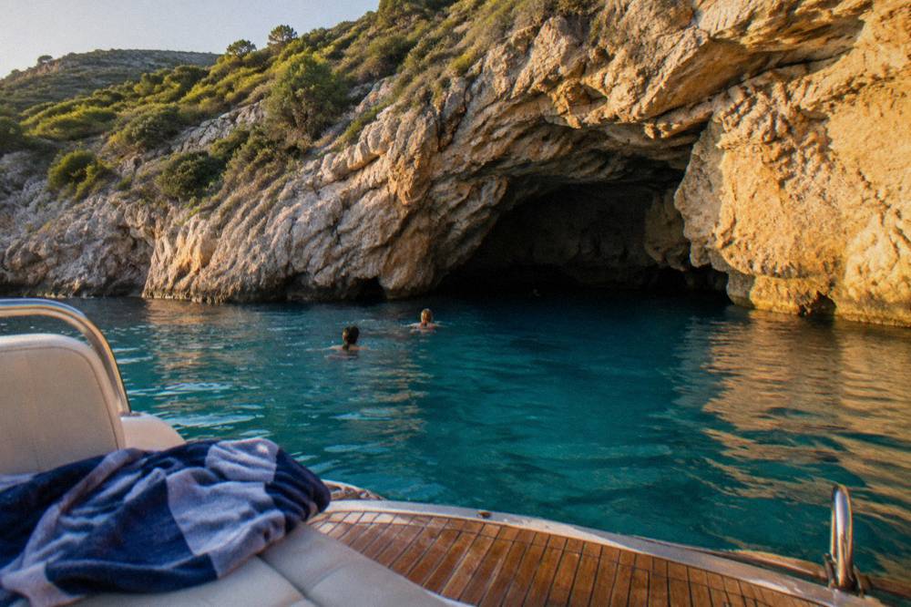 Private speedboat moored beside clear turquoise water near a rocky cave entrance
