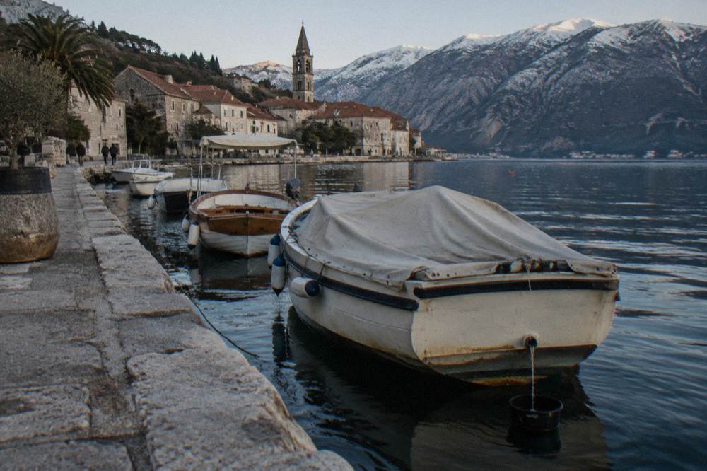 Wooden boats moored along a stone quay in Perast with mountains behind