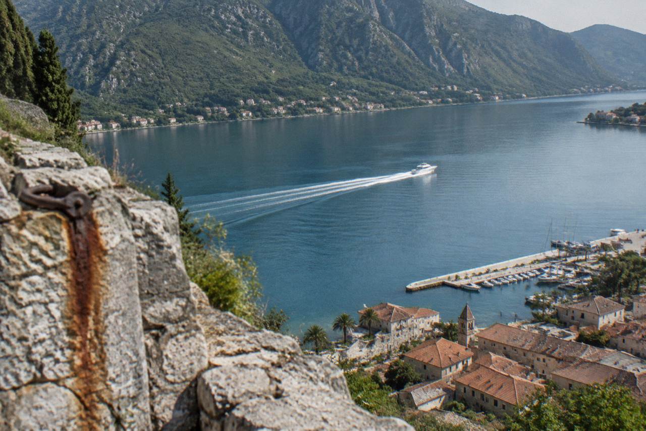 Speedboat crossing calm blue water in the Bay of Kotor toward green hills