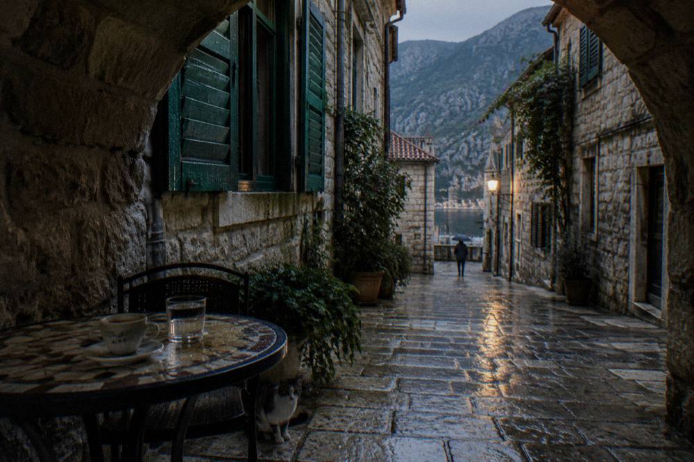 Narrow stone street in Kotor Old Town with shuttered buildings and a cafe table