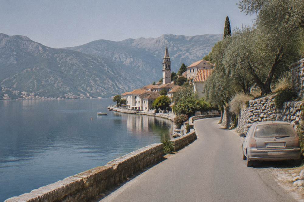 Coastal road curving along the shoreline of the Bay of Kotor with calm water