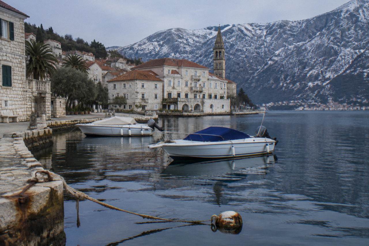 Speedboats moored on the water below the stone buildings and hills of Perast on the Bay of Kotor