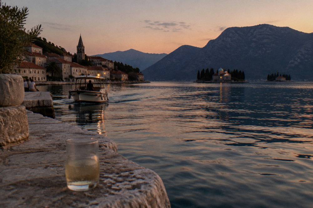 Two small islands in the bay of Kotor seen across still water from a stone quay