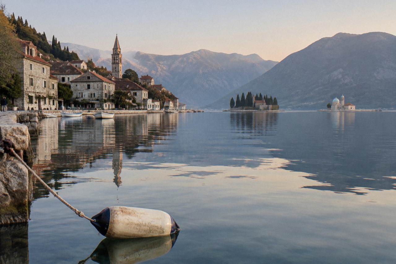 Stone waterfront houses of Perast reflected in calm bay water with two small islands offshore