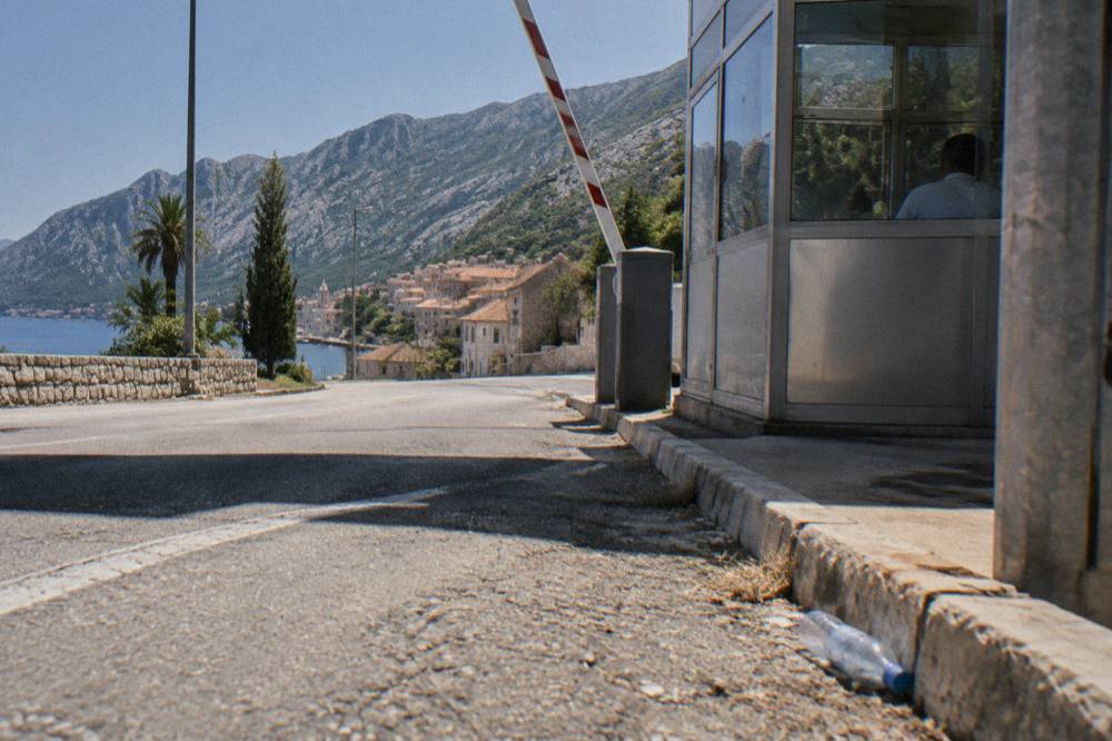 Roadside border control booths with barrier arms and signage beside a dry hillside