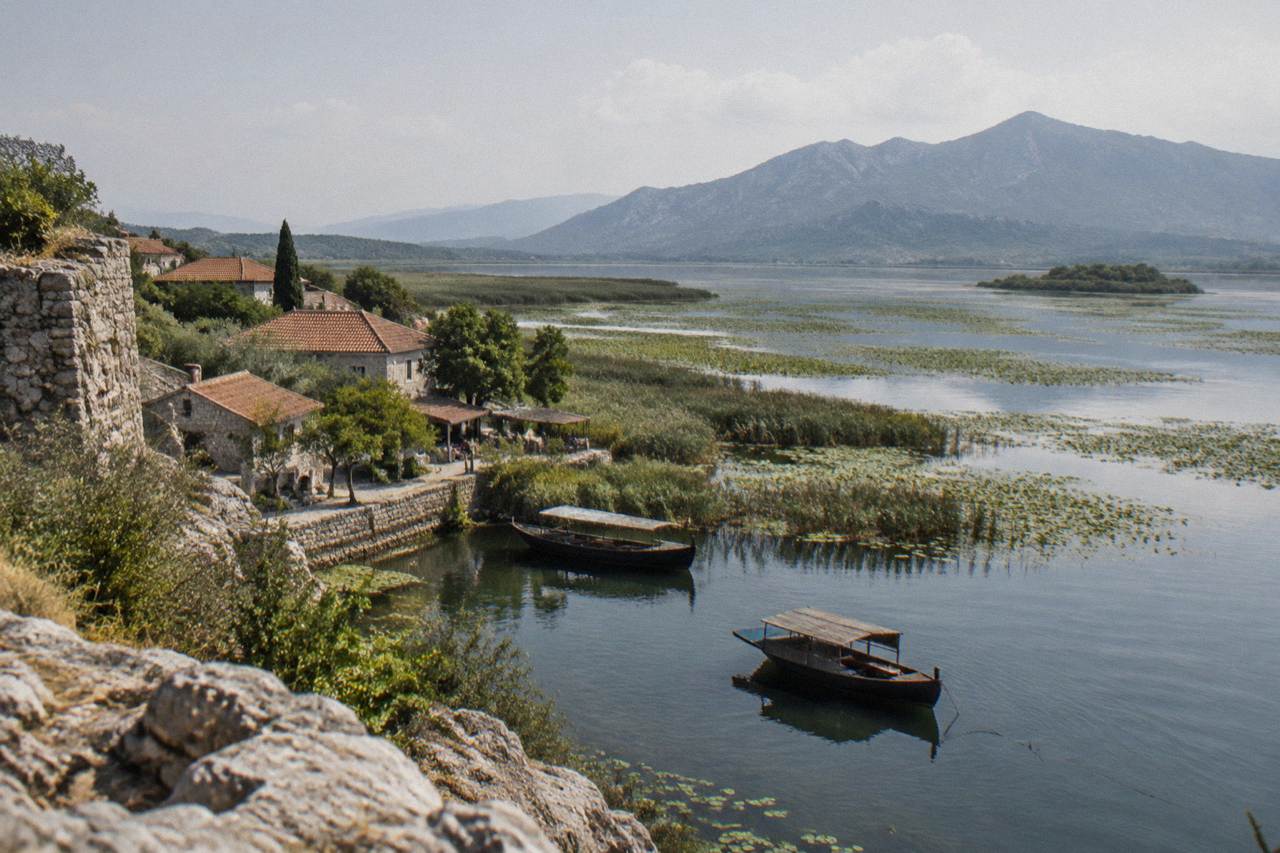 Wide view of Lake Skadar with wooden boats near the shore and hills in the distance