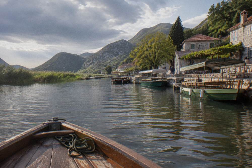 Wooden tour boats moored at a small stone quay on Lake Skadar with reed beds and hills behind