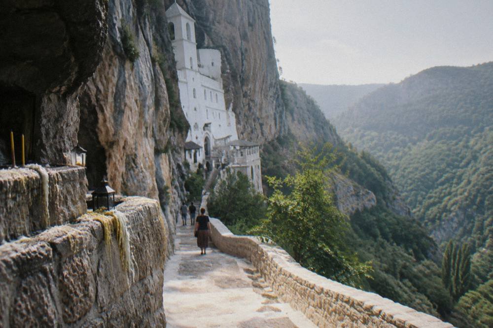 Upper monastery buildings set into the rock face above a forested valley