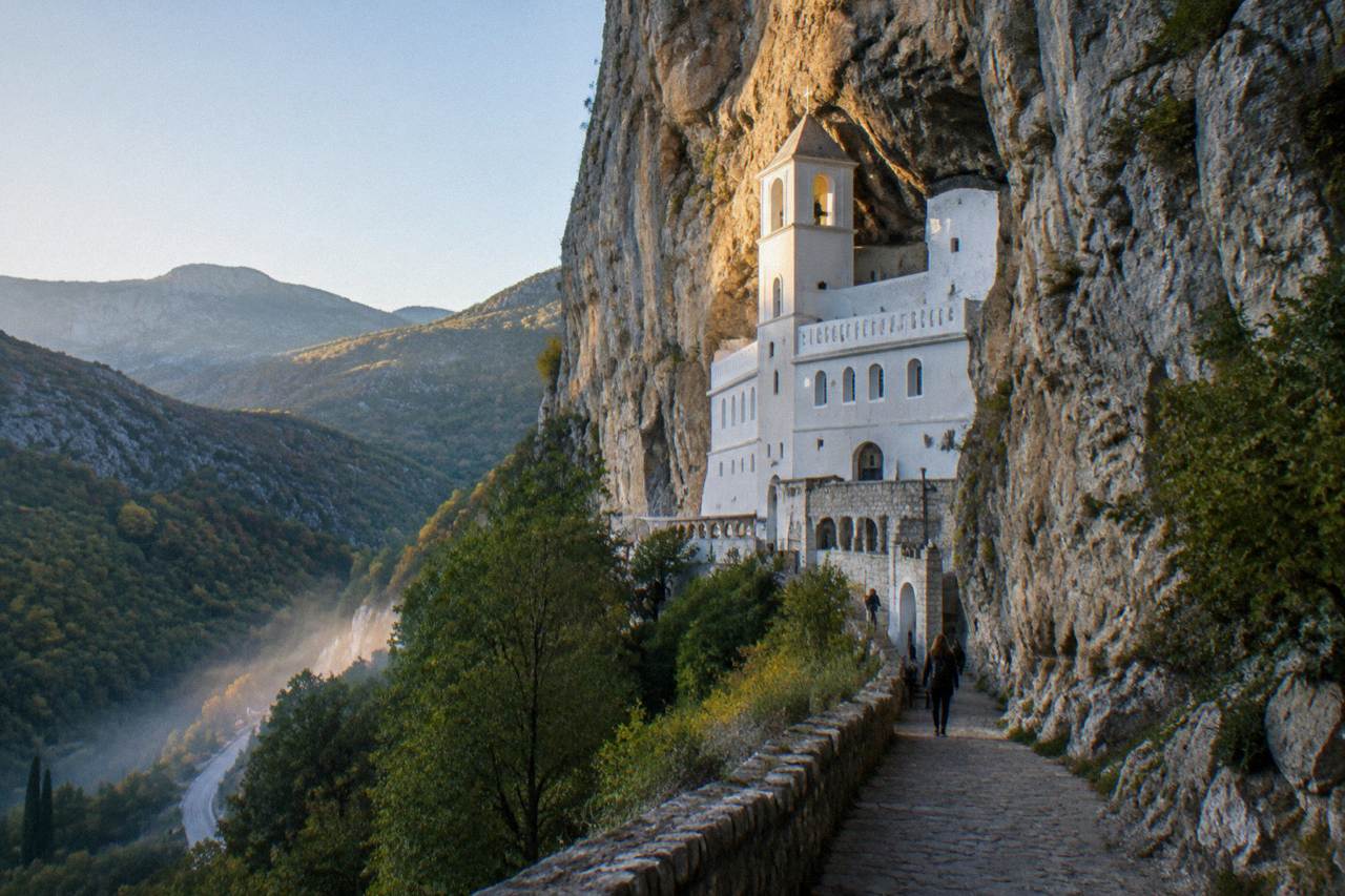 White monastery walls built into a sheer cliff face above a green valley