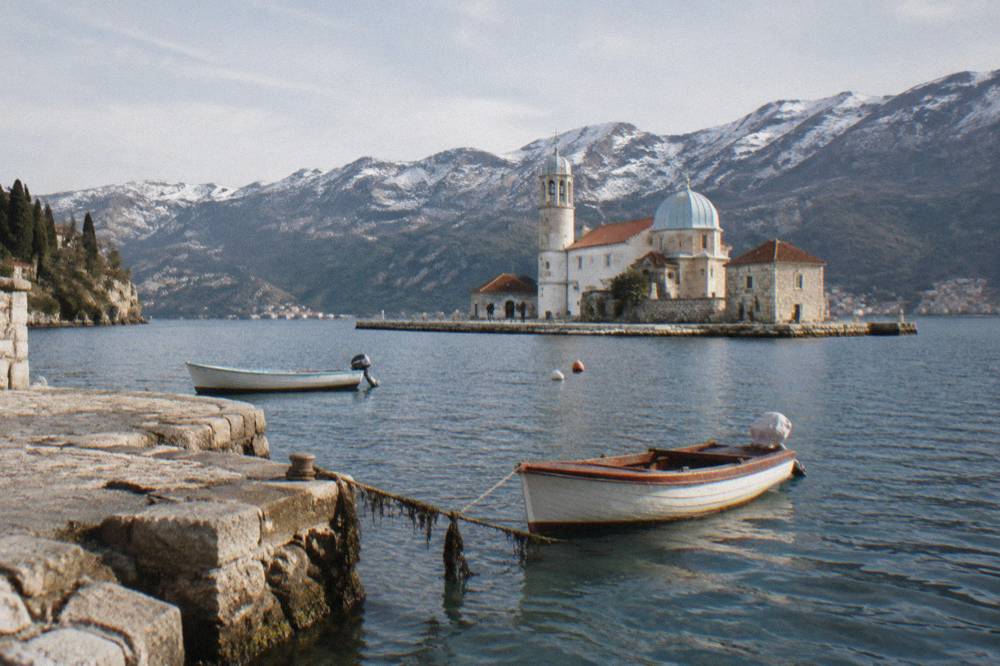 White church tower and low island with boats moored beside it in calm bay water