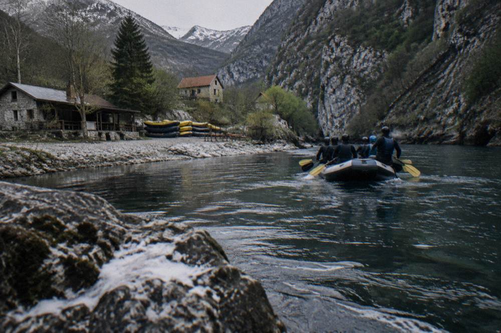 Inflatable raft carrying paddlers along a narrow stretch of river beneath cliffs