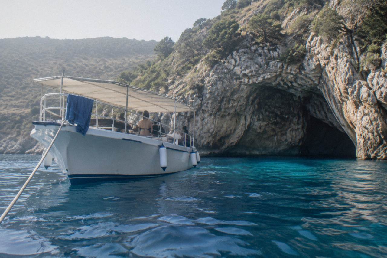 A boat anchored outside a sea cave entrance on a rocky coastline with clear blue water